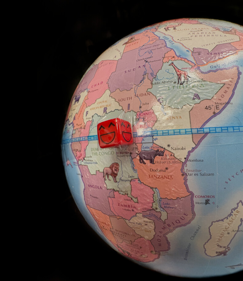 A close-up of a physical globe turned to east Africa, with two small red dice, each with a smiling face drawn on it, resting on the equator over Rwanda and Burundi