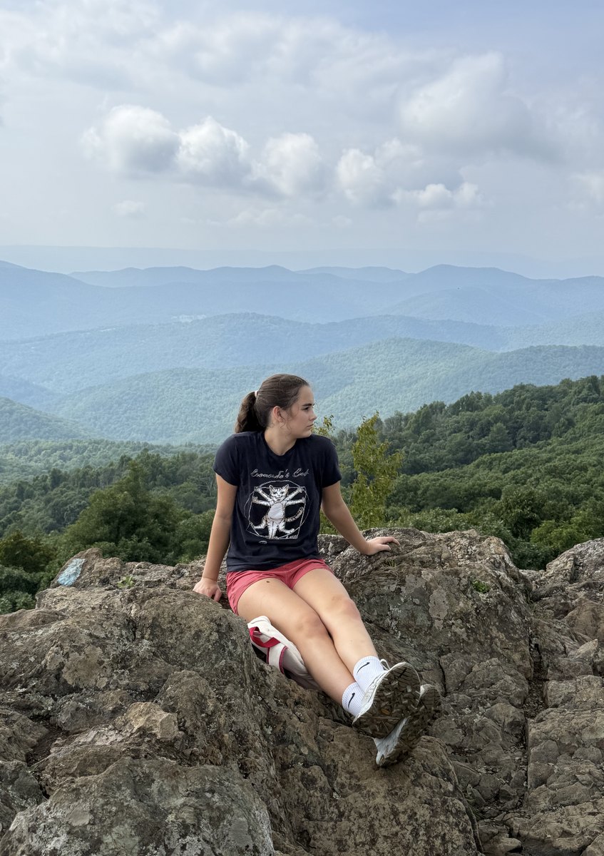 Marie sitting on a rocky overlook, looking out over blue ridges of forest